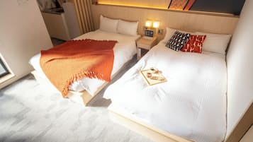 A hotel room with two beds, a small bedside table with a lamp, and a window.