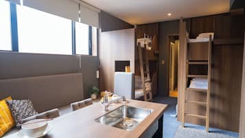 A modern kitchen with a built-in sink, a dining table, and a bunk bed with a ladder.