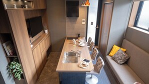 A compact kitchenette with a sink, countertop, and built-in TV. A dining area with chairs and a table is adjacent to the kitchen. - ORI Rokkaku (Kyoto)