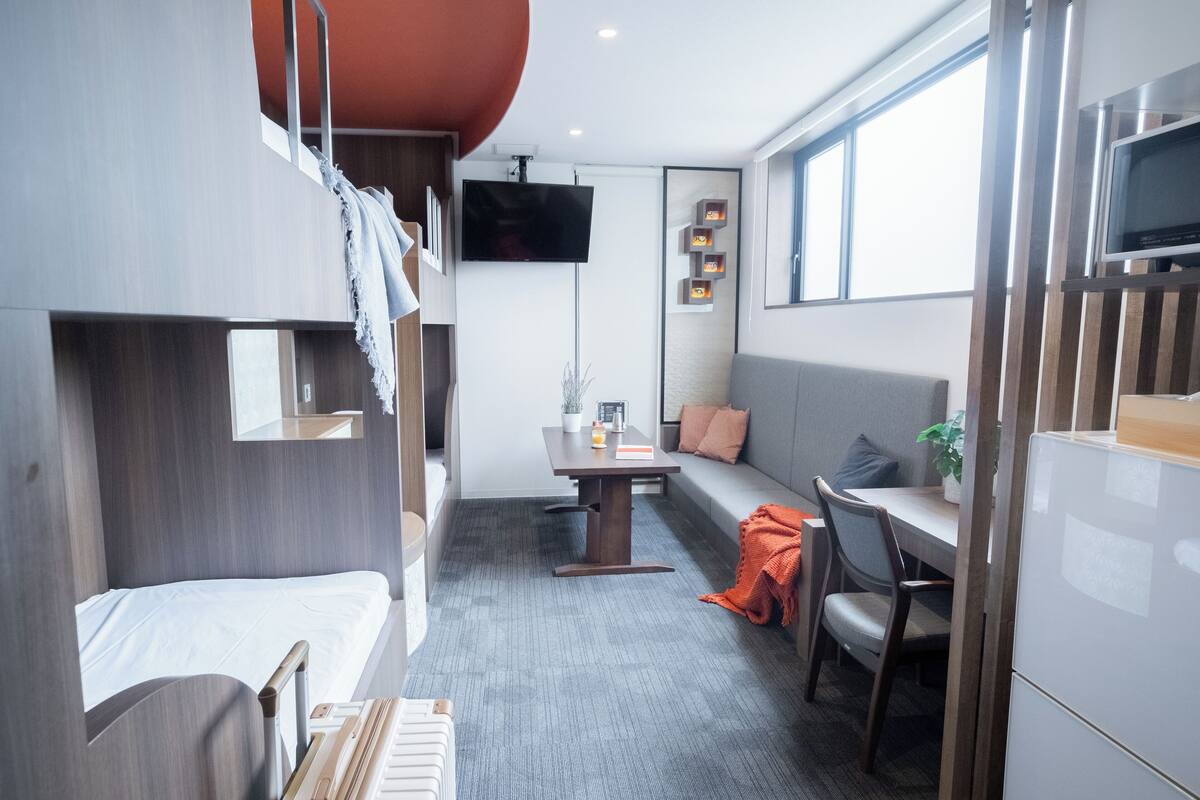 A compact room with bunk beds, a sofa, a dining table, and a TV.