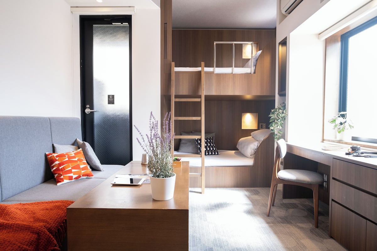 A modern room with a sofa, a desk, a ladder, and a window.