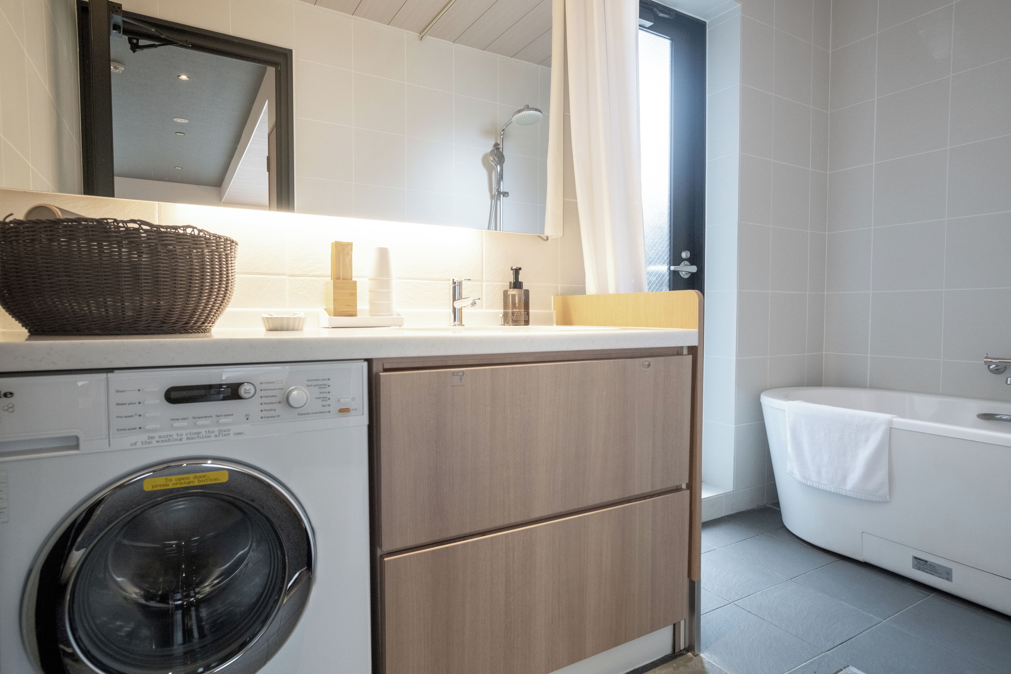 Een kleine badkamer met een wasmachine, een bad en een douche.