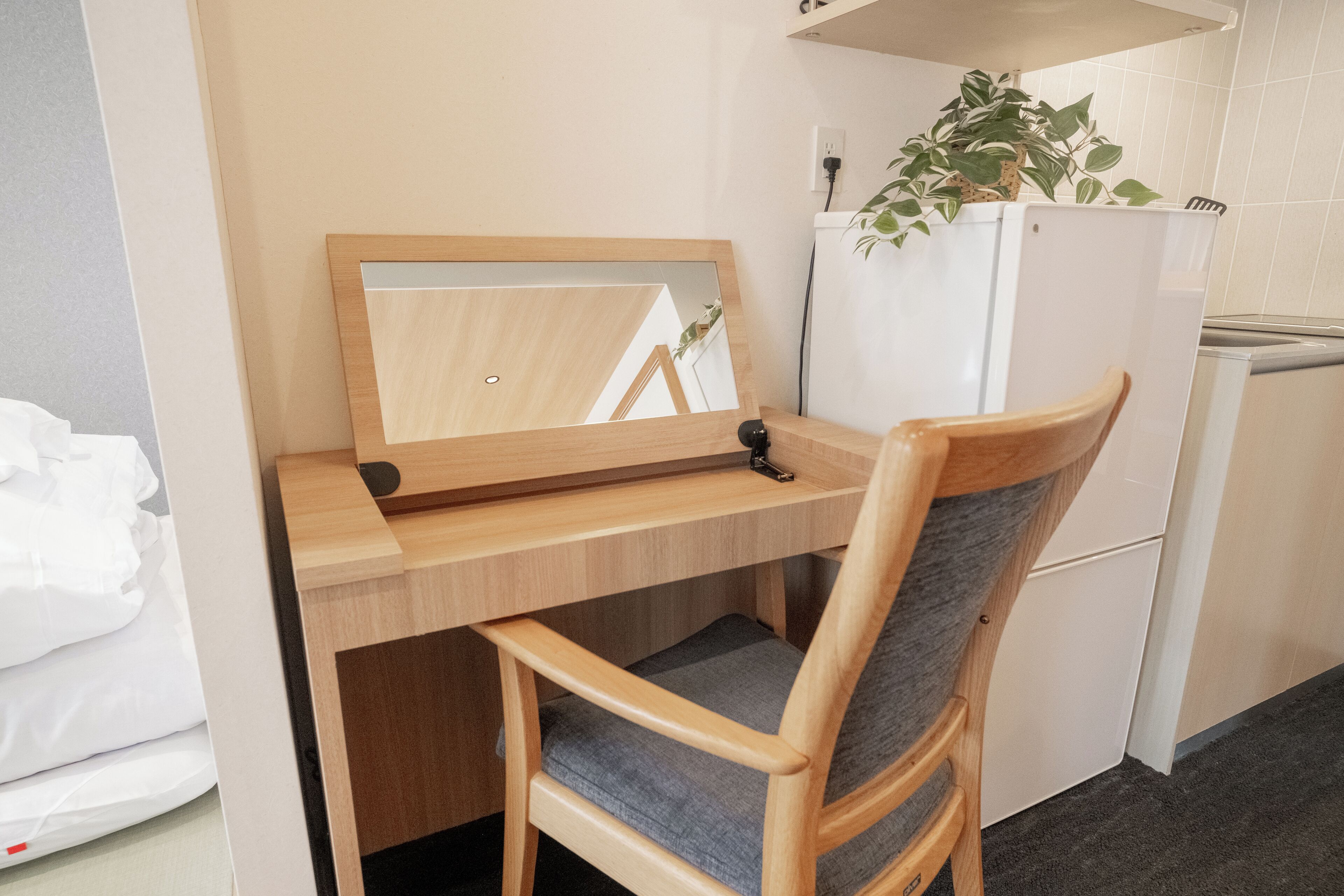 Una kitchenette compacta con un escritorio de madera, una silla, un espejo, un refrigerador y una planta en maceta.
