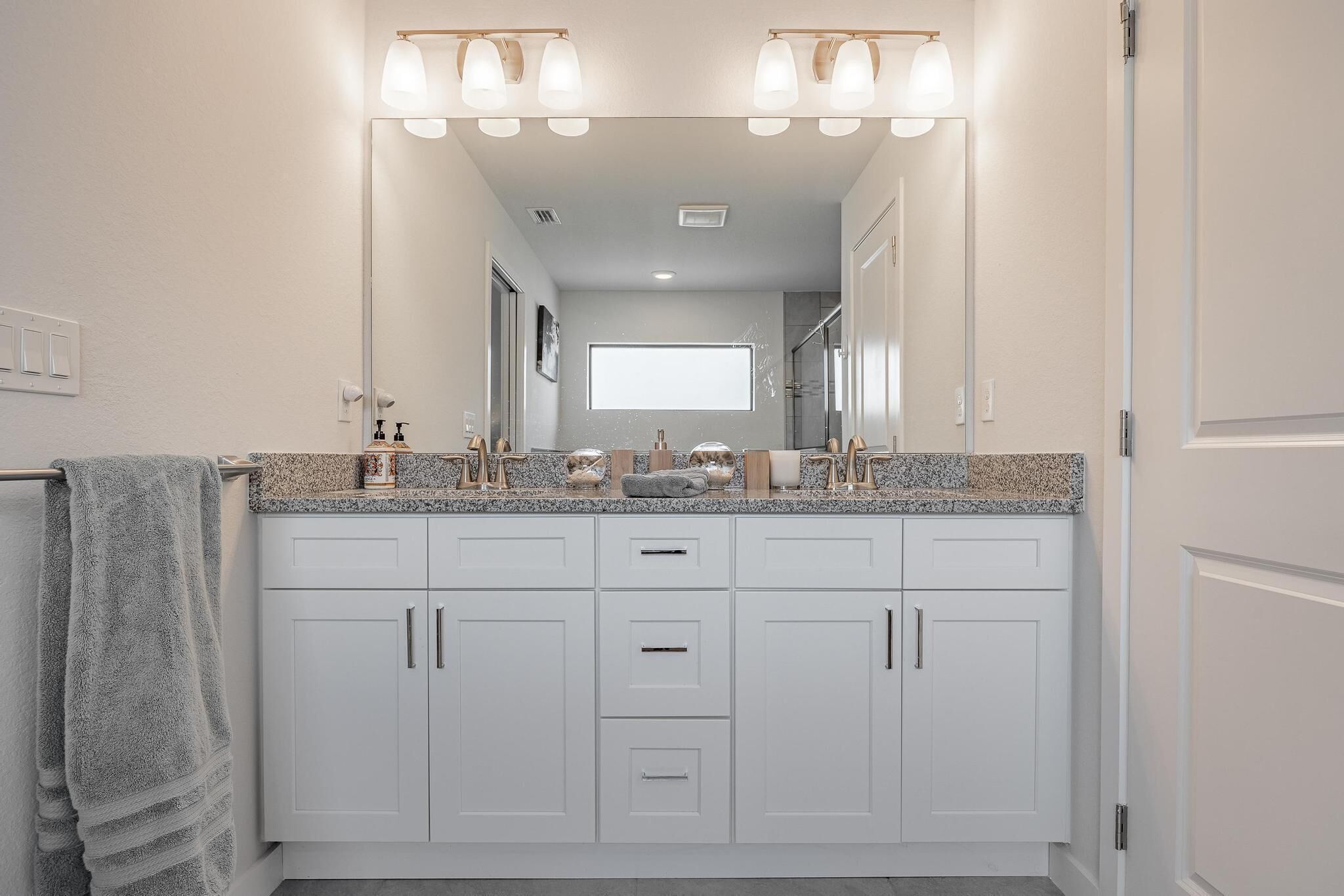 A modern bathroom with a large mirror, white cabinets, and a granite countertop.