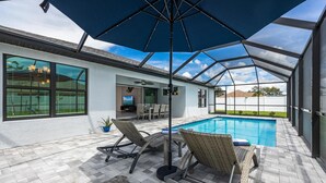Un espace extérieur abrité avec une piscine, des chaises longues et un grand parasol.