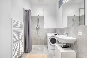 Enjoy a refreshing shower in the walk-in shower with a glass door, a washing machine, and a standalone sink.