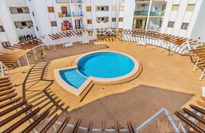 A pool area with sun loungers arranged in a semi-circle around a central pool, surrounded by a multi-story building with balconies and windows. - Inftour Eurosol Apartamento (Calp)