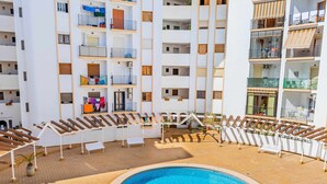 Un hotel de varios pisos con una piscina central rodeada de sillas de descanso y una terraza con baldosas.