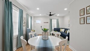 Un comedor con una mesa redonda, sillas blancas, un ventilador de techo y un mantel con estampado azul y blanco.