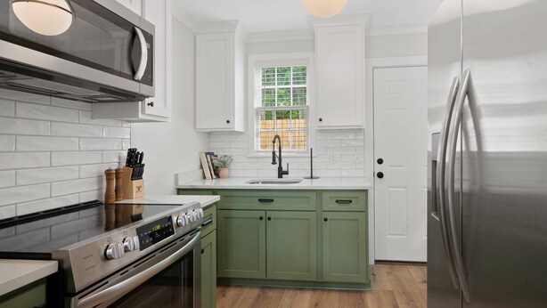Una cocina moderna con armarios blancos, una isla verde, electrodomésticos de acero inoxidable y una ventana con vistas.