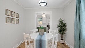 Un comedor con una mesa redonda, sillas blancas, camino de mesa azul e impresiones botánicas enmarcadas en la pared.