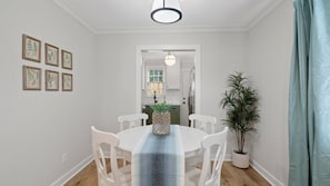 Ein Essbereich mit einem runden Tisch, weißen Stühlen, einer blauen Tischläufer und gerahmten Pflanzenbildern an der Wand.
