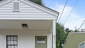 Una casa de un piso con puerta verde, un pequeño porche con banco y valla de madera.
