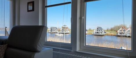 A room with a large window overlooking a canal with boats and houses.