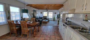 Une cuisine avec un coin repas, des poutres apparentes en bois au plafond et une vue sur l’extérieur.