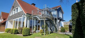 Une maison à deux étages, avec un toit recouvert de tuiles rouges, un balcon et un escalier menant à l’étage supérieur.