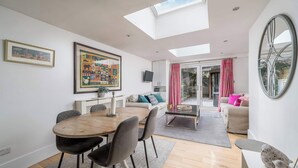 A modern living room with a dining area, a large painting, a TV, and a view through a glass door. - Gorgeous flat with garden in Battersea (London)