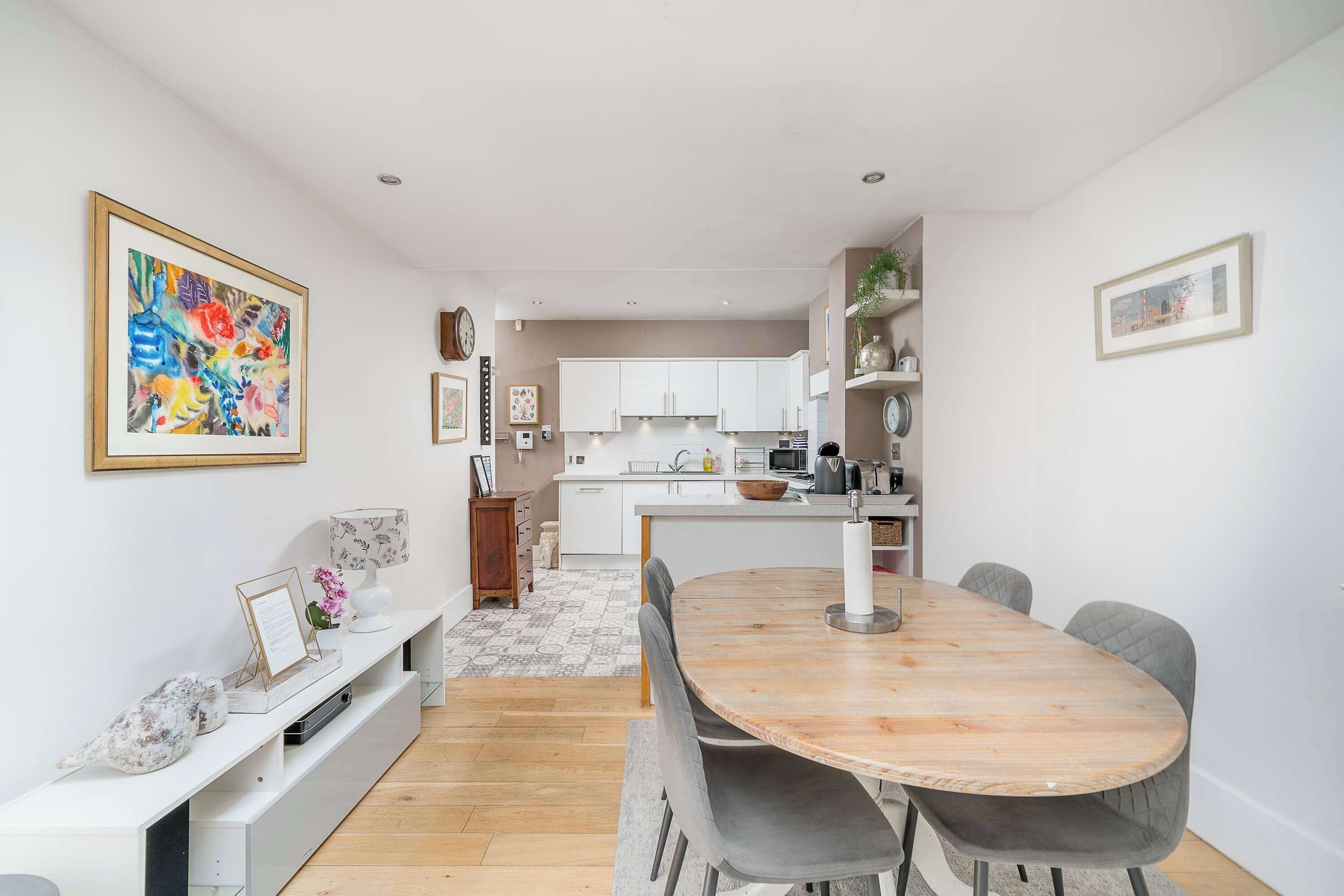 A modern kitchen with white cabinets, a central island, and a dining area with a wooden table and grey chairs.