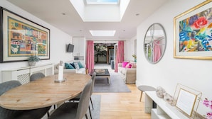A modern living room with a skylight, a dining area with a wooden table, and a view into the adjacent room. - Gorgeous flat with garden in Battersea (London)