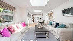 A modern living room with a sofa, a coffee table, and a dining area in the background. - Gorgeous flat with garden in Battersea (London)