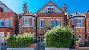A row of red brick terraced houses with white window frames and a central entrance. - Gorgeous flat with garden in Battersea (London)
