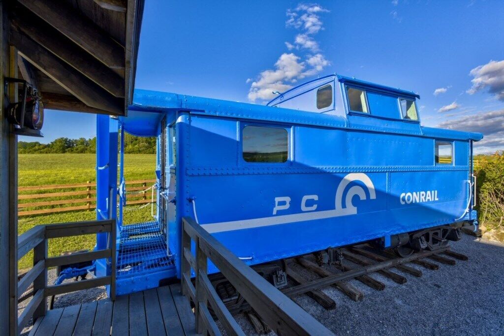 Een blauwe Conrail kluiswagons met een klein hutje en een trap naar de deur.