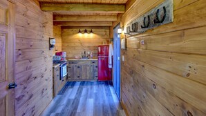 A wooden cabin interior with a kitchen area, including a red refrigerator, wooden cabinets, and a wooden ceiling. - The Caboose | Mtn Views | Farm Animals + Sauna (Canajoharie)