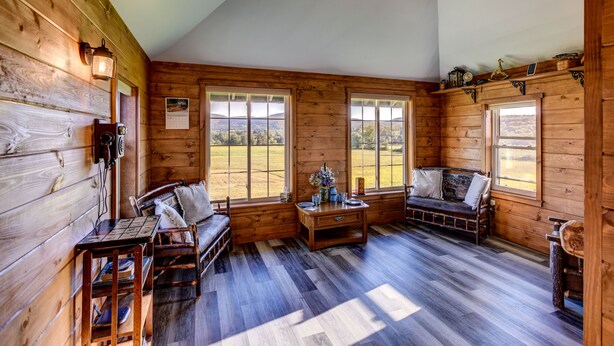 A wooden cabin interior with a wooden bench, a small table with a vase, and a window with a view of a field. - The Caboose | Mtn Views | Farm Animals + Sauna (Canajoharie)