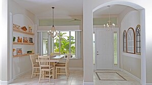 A spacious room with a dining table and chairs, a chandelier, and a view of greenery outside.