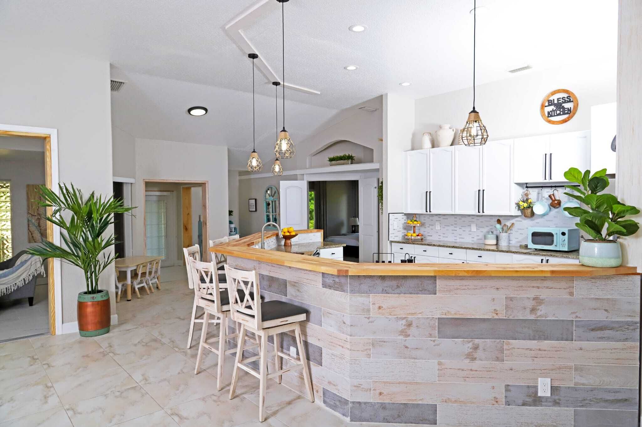 A modern kitchen with a central island, white cabinets, and pendant lighting.