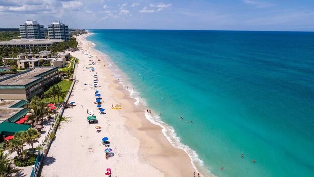 A beach with a row of beach umbrellas, a sandy shore, and a clear blue ocean.