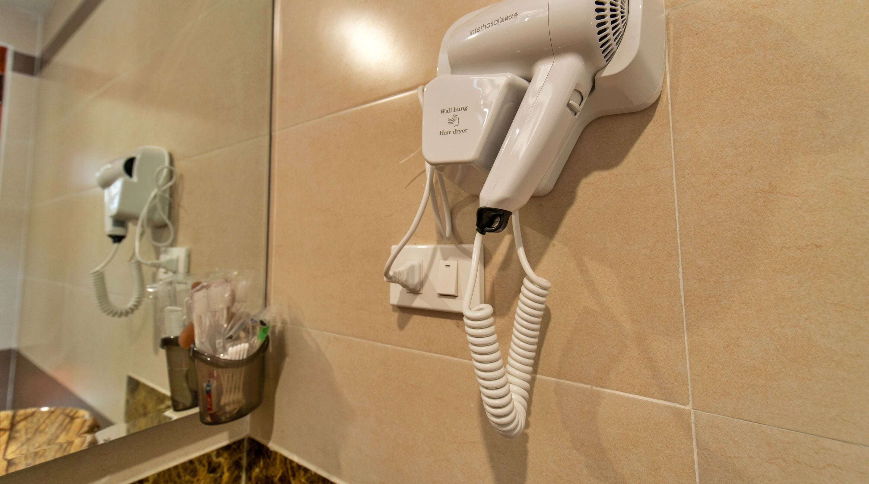 A hair dryer mounted on a wall with a cord, a phone, and a small container with toiletries.