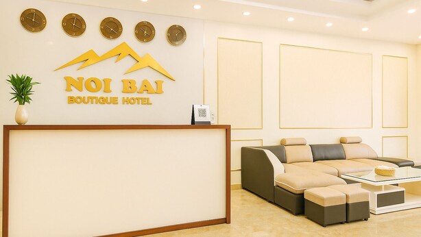 A reception area with a reception desk, a sofa set, and a wall with clocks and a logo for Noi Bai Boutique Hotel. - S79 Noi Bai Airport Hotel (Hanoi)