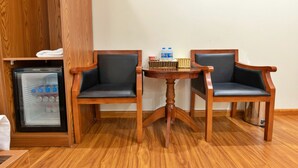 A compact hotel room with a wooden cabinet, a minibar, two wooden chairs, a small round table, and a water dispenser. - S79 Noi Bai Airport Hotel (Hanoi)