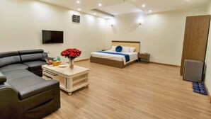 A modern hotel room with a sofa, a bed with a wooden headboard, a bedside table, a flat-screen TV mounted on the wall, and a small wooden cabinet. - S79 Noi Bai Airport Hotel (Hanoi)