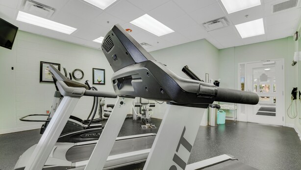 Een sportschool met loopbanden, fitnessapparatuur en een witte muur met ingelijste foto's.