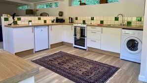 A compact kitchen with white cabinets, a built-in oven, a washing machine, and a patterned rug on the floor. - Romantic hideaway cottage, near Bridport, Dorset (Bridport)
