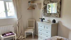 A bedroom with a large bed, a chair, a dresser, a radiator, and a window with curtains. - Romantic hideaway cottage, near Bridport, Dorset (Bridport)