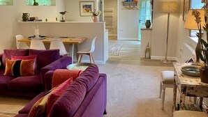 A modern living room with a purple sofa, a dining area with a table and chairs, and a kitchen in the background. - Romantic hideaway cottage, near Bridport, Dorset (Bridport)