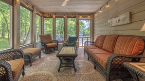 A covered porch with wicker furniture, a ceiling fan, and large windows overlooking a wooded area. - The Aspen Cottage by Innsbrook Vacations! (Innsbrook)