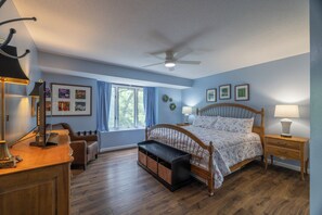 Ein Schlafzimmer mit Bett, Nachttischen, Schreibtisch, Stuhl, Fenster und Deckenventilator.