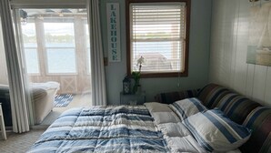 Una camera da letto con un letto, una finestra con persiane, un cartello con su scritto “LAKEHOUSE” e vista sul lago.