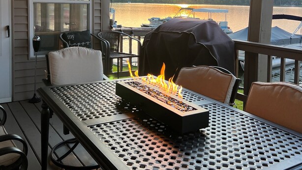 Un patio coperto con tavolo, sedie, barbecue e vista sul lago al tramonto.