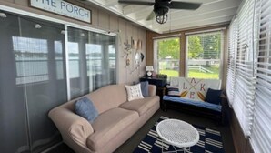 Un soggiorno accogliente con un divano beige, un tavolino rotondo e una ventola a soffitto. Un cartello sopra recita "THE PORCH".