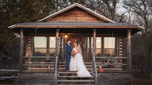 A wooden cabin with a porch, a stone wall in the foreground, and a wooden staircase leading up to the porch. - The Cabins at Angel Springs - Woodland (Georgetown)