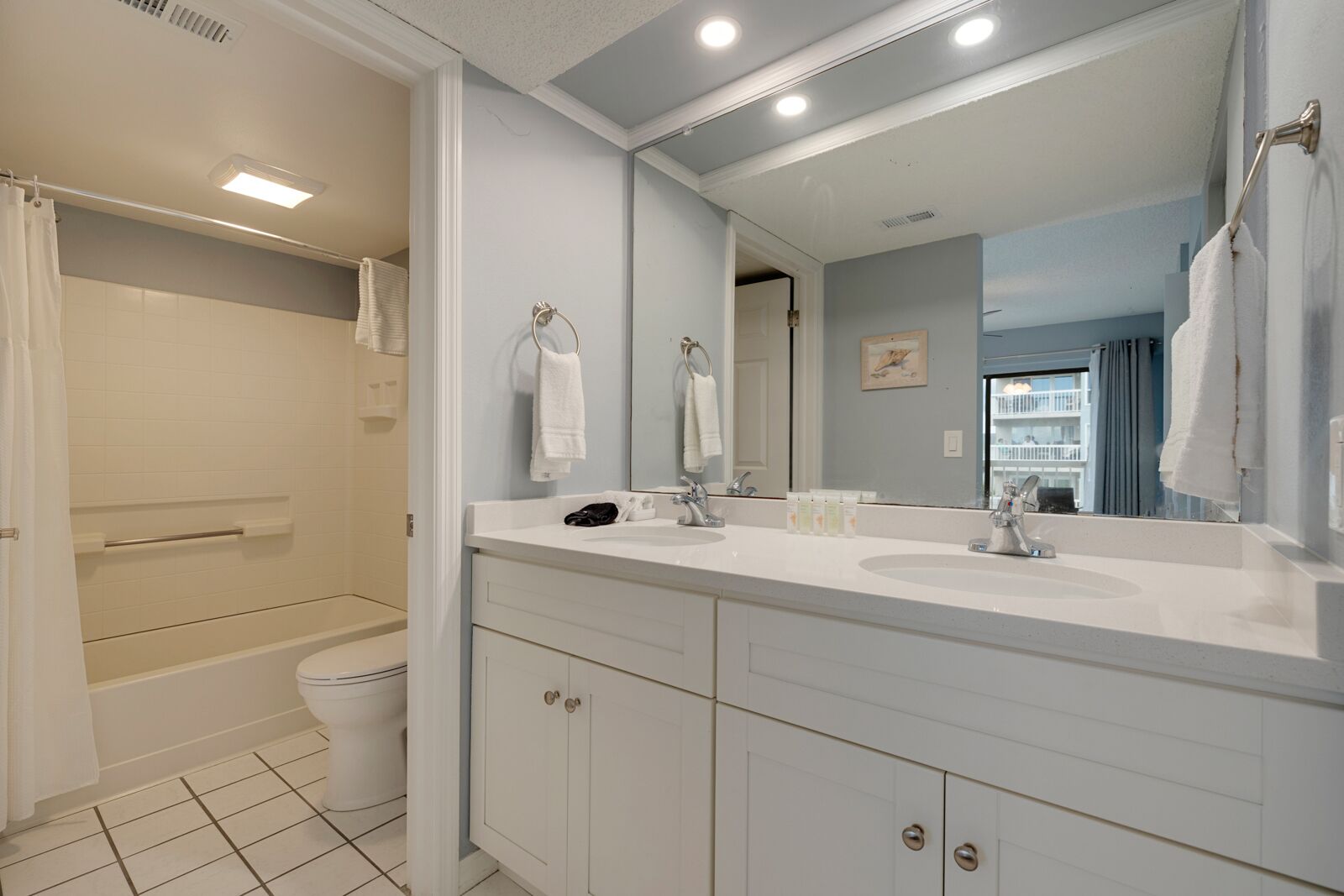 A modern bathroom with a bathtub, a toilet, and a sink. There are towels hanging on hooks and a large mirror above the sink.