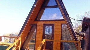 A wooden cabin with a triangular roof, large windows, and a wooden deck.