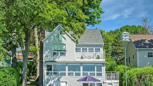 Une maison à deux étages dotée d’un balcon, d’un garage et d’un patio aménagé avec des sièges d’extérieur.