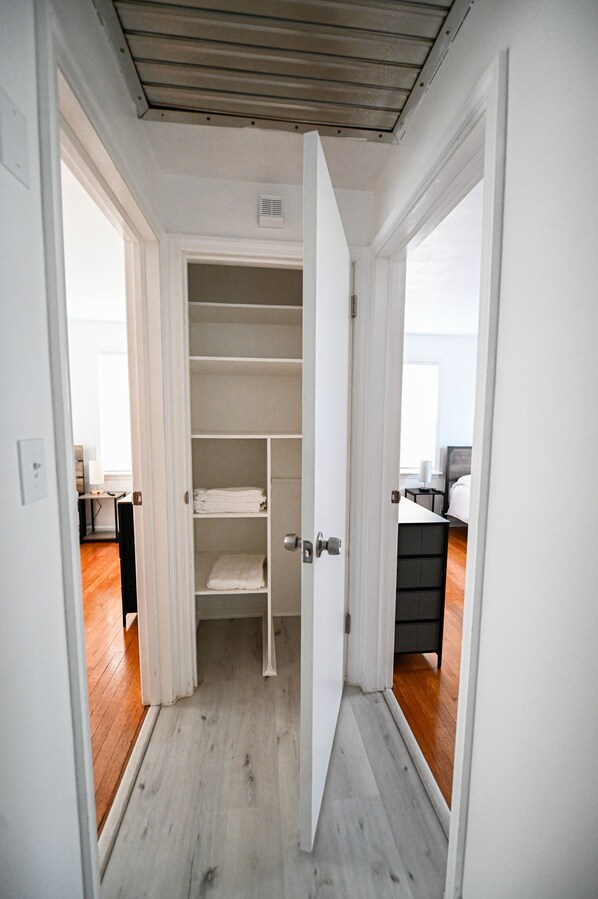 Un couloir étroit avec une porte blanche donnant sur une pièce où se trouvent un lit et un bureau.