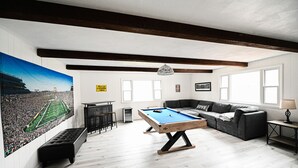 Een kamer met een pooltafel, een bank, een lange bank en een grote muurschildering met sportthema.